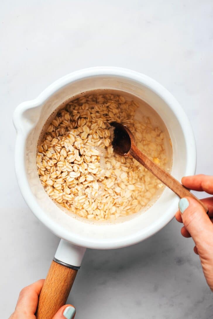 A woman’s hands stir rolled oats and water in a small saucepan.