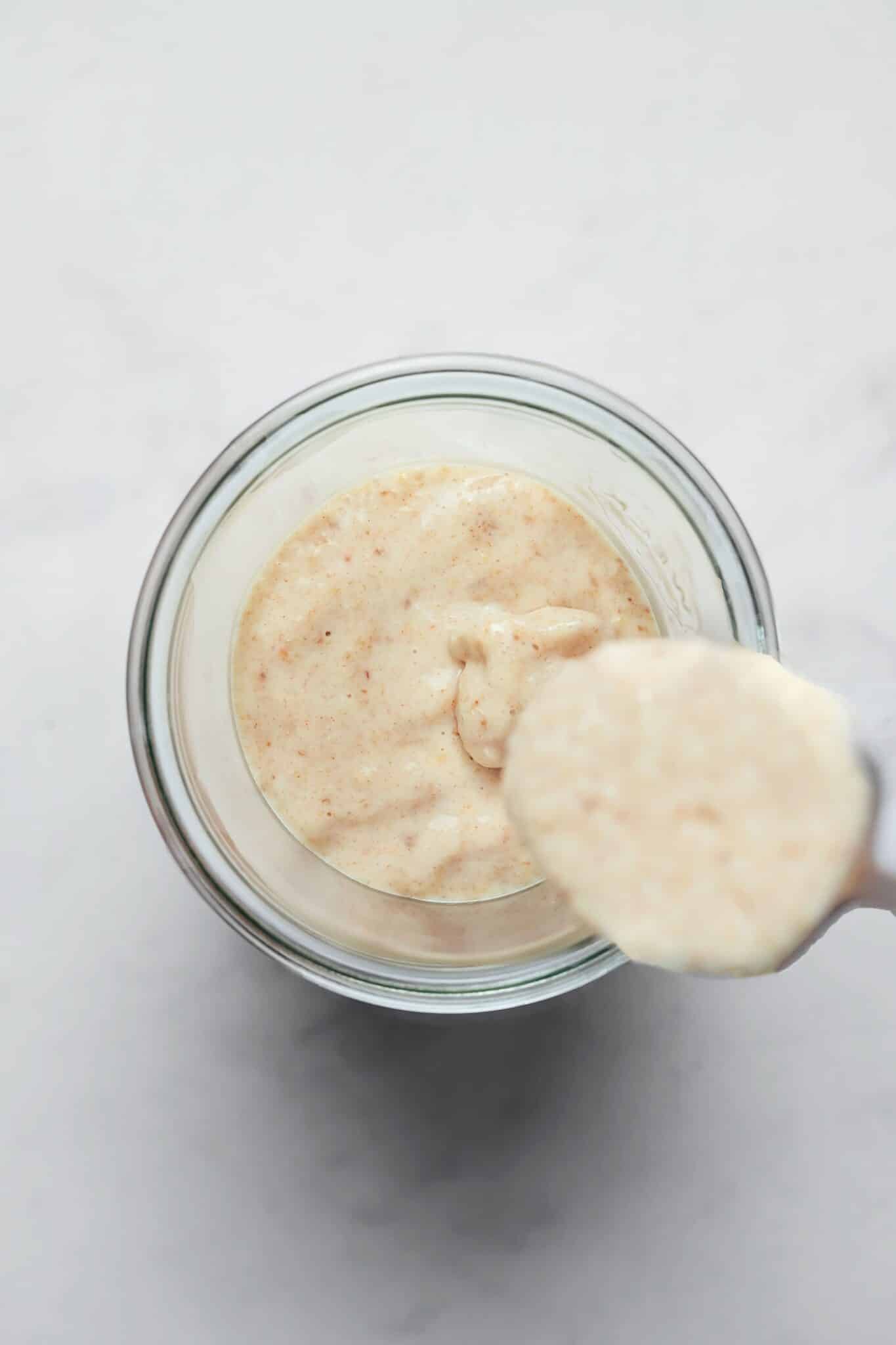 Creamy blended oats being spooned into a glass jar.