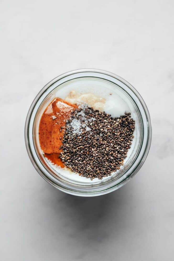 Chia seeds, nut butter, yogurt, and flaky salt added to a jar of blended oats.