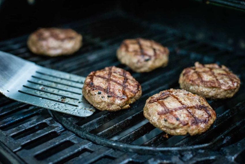 Grilling lamb burgers with a spatula.