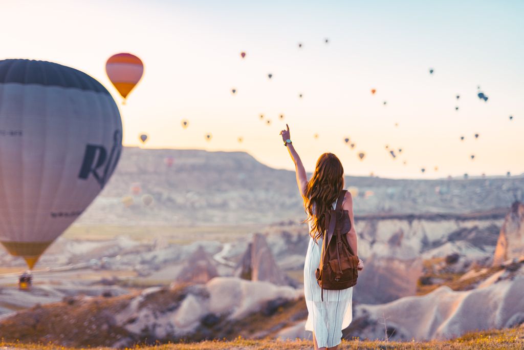 A woman points at colorful hot air balloons over Cappadocia at sunrise. Put this on your travel bucket list