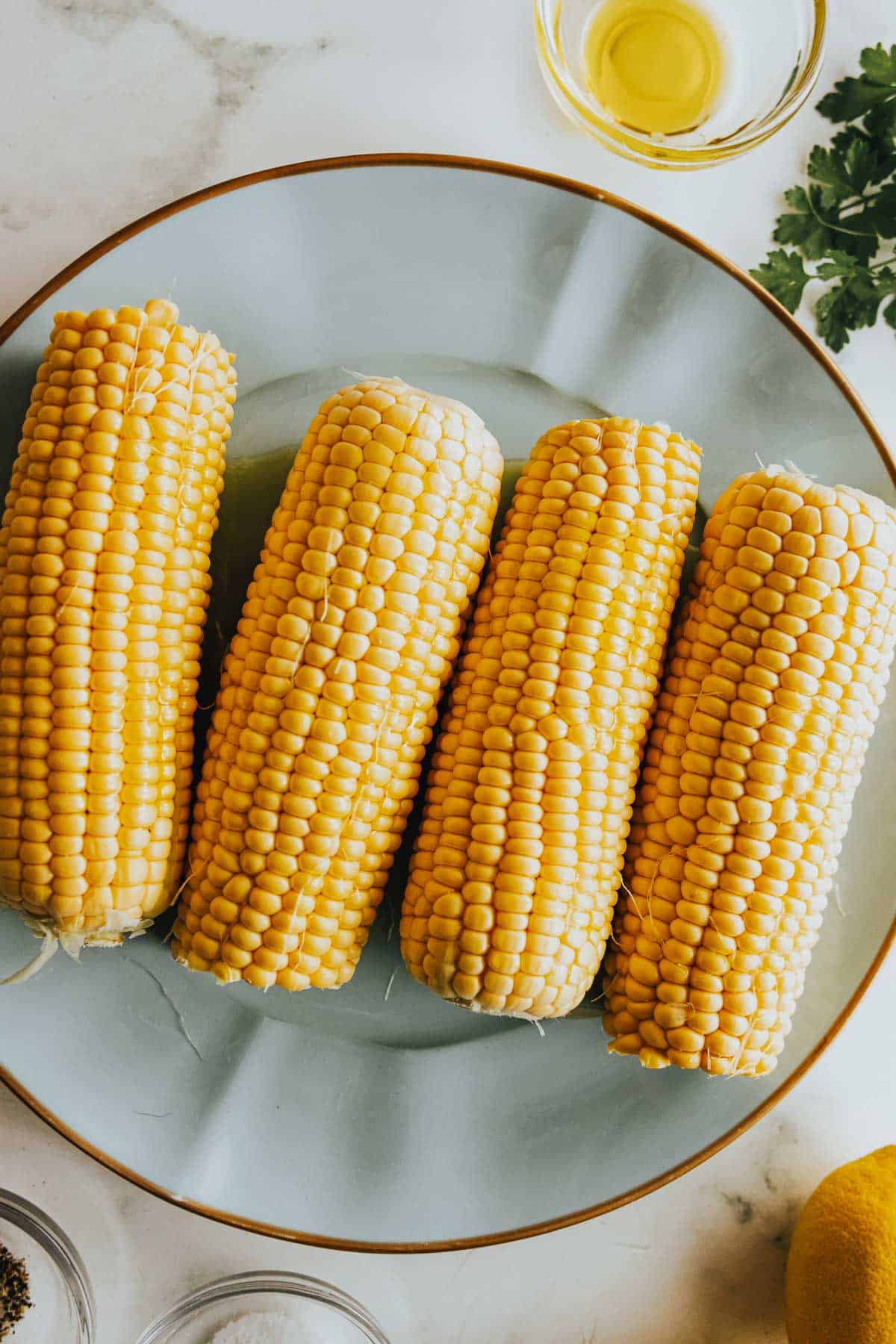 Corn on the cob on a plate with lemons and herbs.