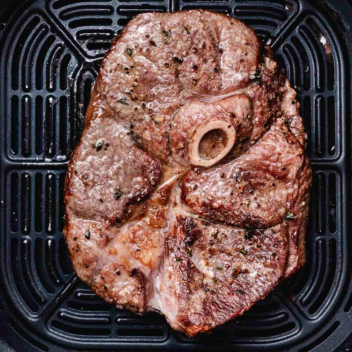 Air-fried bone-in lamb leg steak browned in the air fryer basket.