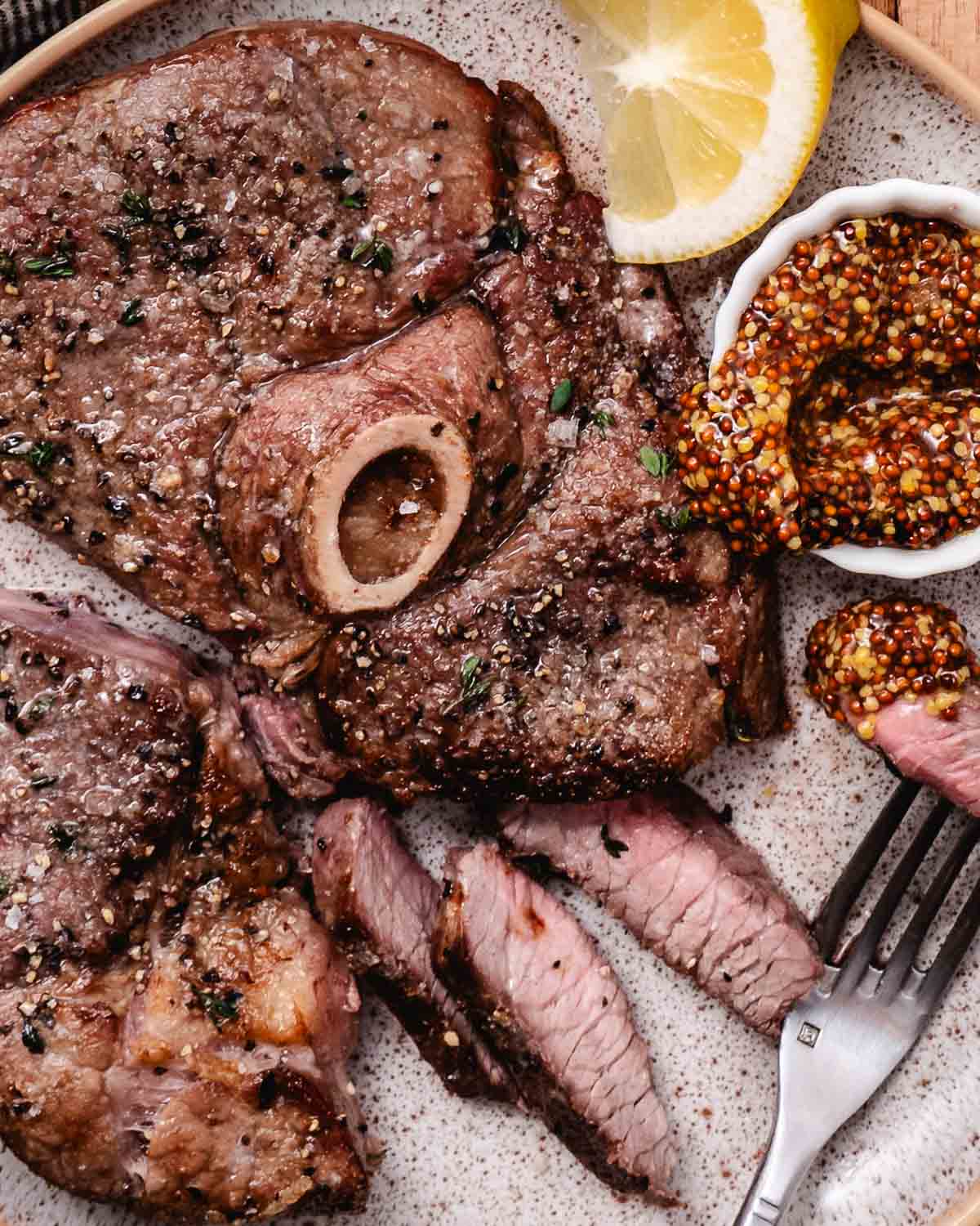Sliced air fryer lamb leg steak served with whole-grain mustard and lemon.