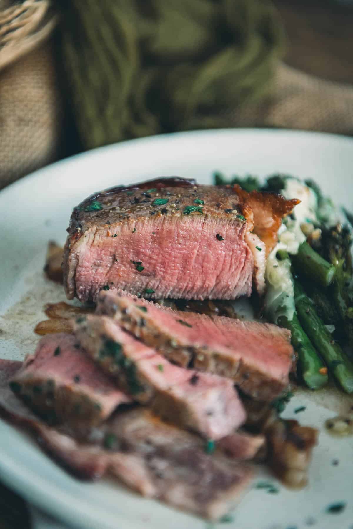 Showing a bacon-wrapped filet mignon, sliced exposing a rosy pink medium rare center.