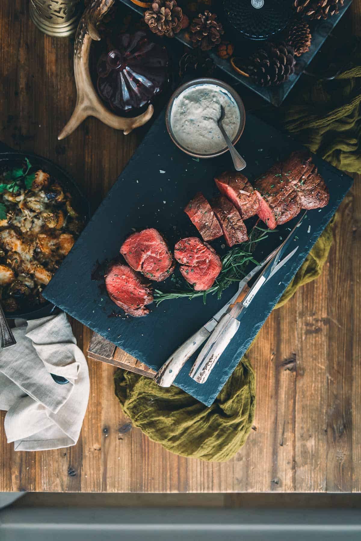 Overhead rustic table of oven roasted beef tenderloin with horseradish cream and brussels sprouts.
