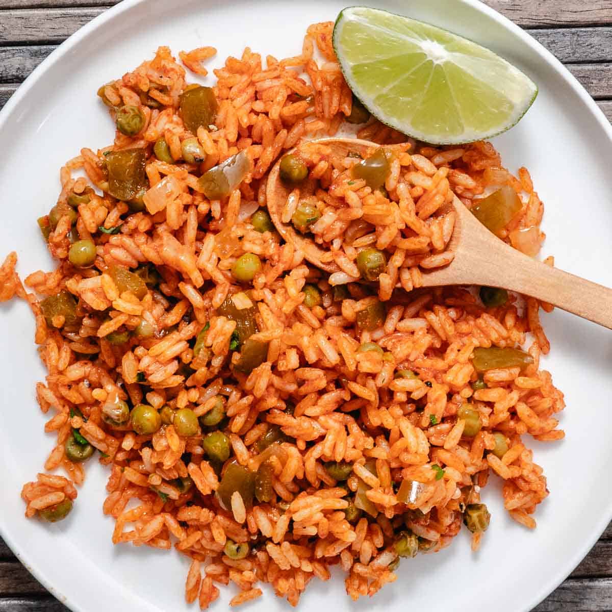 Spanish rice with peas, green bell pepper, and onion served on a white plate with a lime wedge.