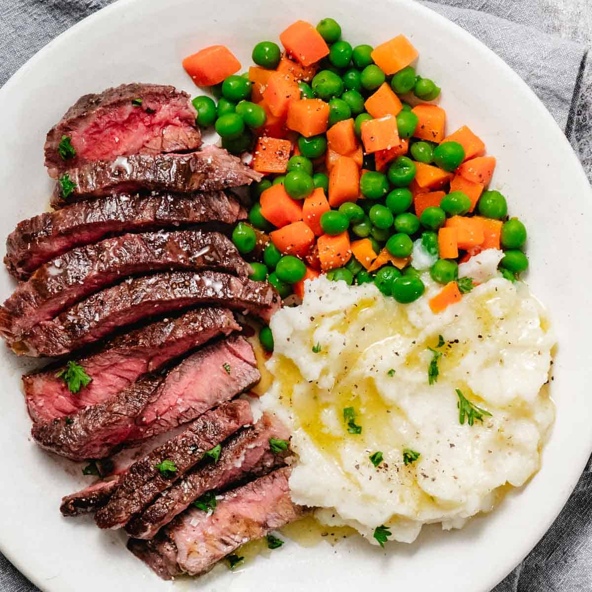 pan seared chuck steak with mashed potatoes and peas and carrots.
