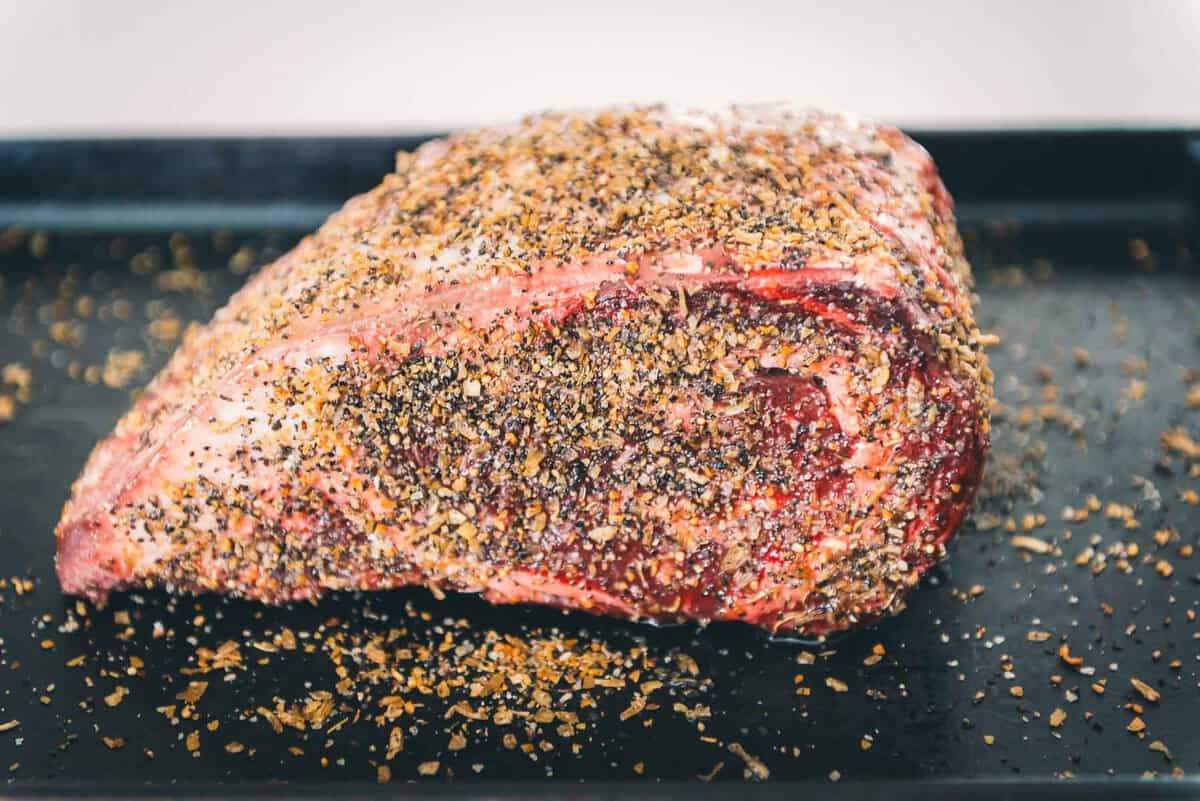 A boneless rib roast on a black tray with seasonings on it.