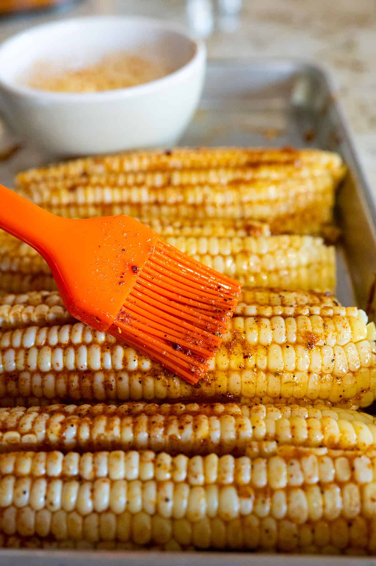 brushing butter and spices on raw corn.