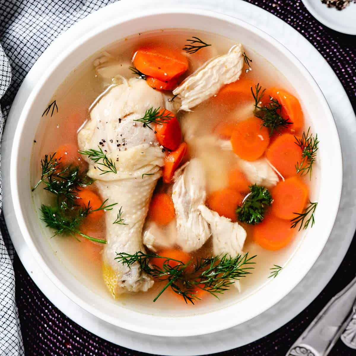 chicken soup with carrots and a drumstick in a white bowl.