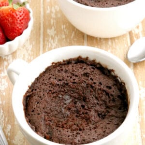 two gluten-free chocolate mug cakes with strawberries in the background