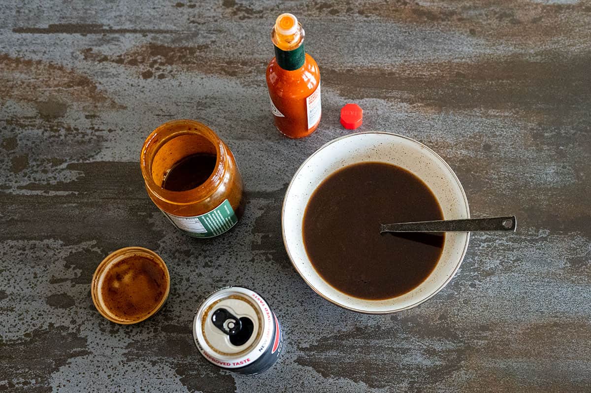 bowl of cola bbq sauce along with jar of sauce, can of cola and bottle of hot sauce.