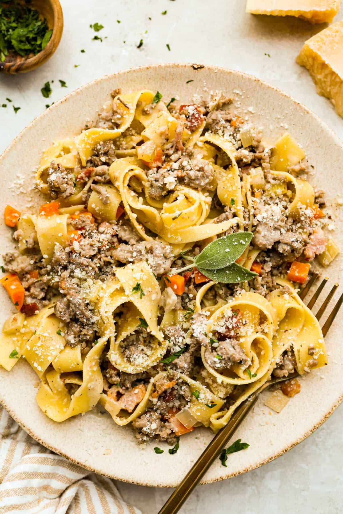No tomatoes, no red sauce, just a rich, savory white bolognese loaded with beef, pork, bacon, white wine, and plenty of Parmesan. Tossed with noodles, it’s a fun and seriously delicious twist on classic Bolognese. Plated white bolognese dusted with parmesan cheese and garnished with fresh sage.