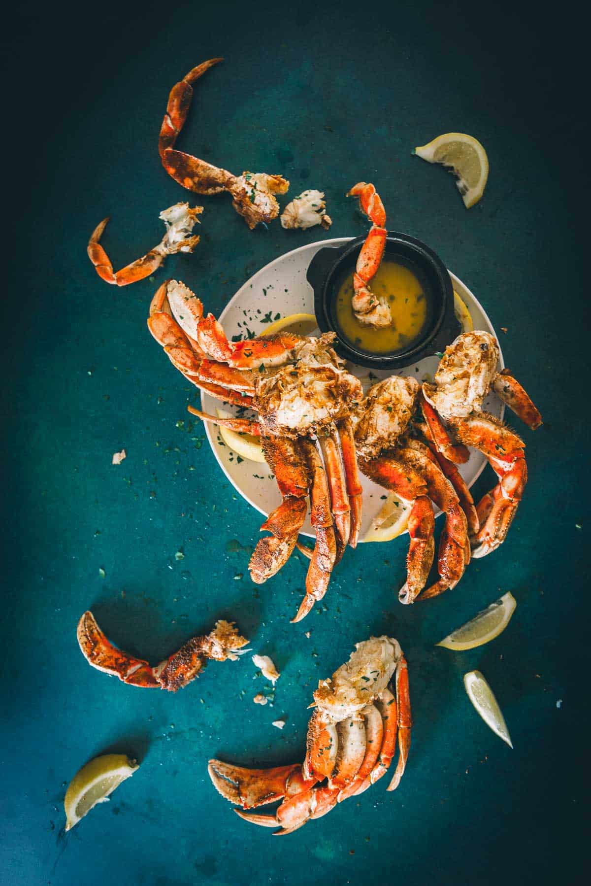 Overhead shot of steamed crab clusters on a surface with lemon wedges and butter. 
