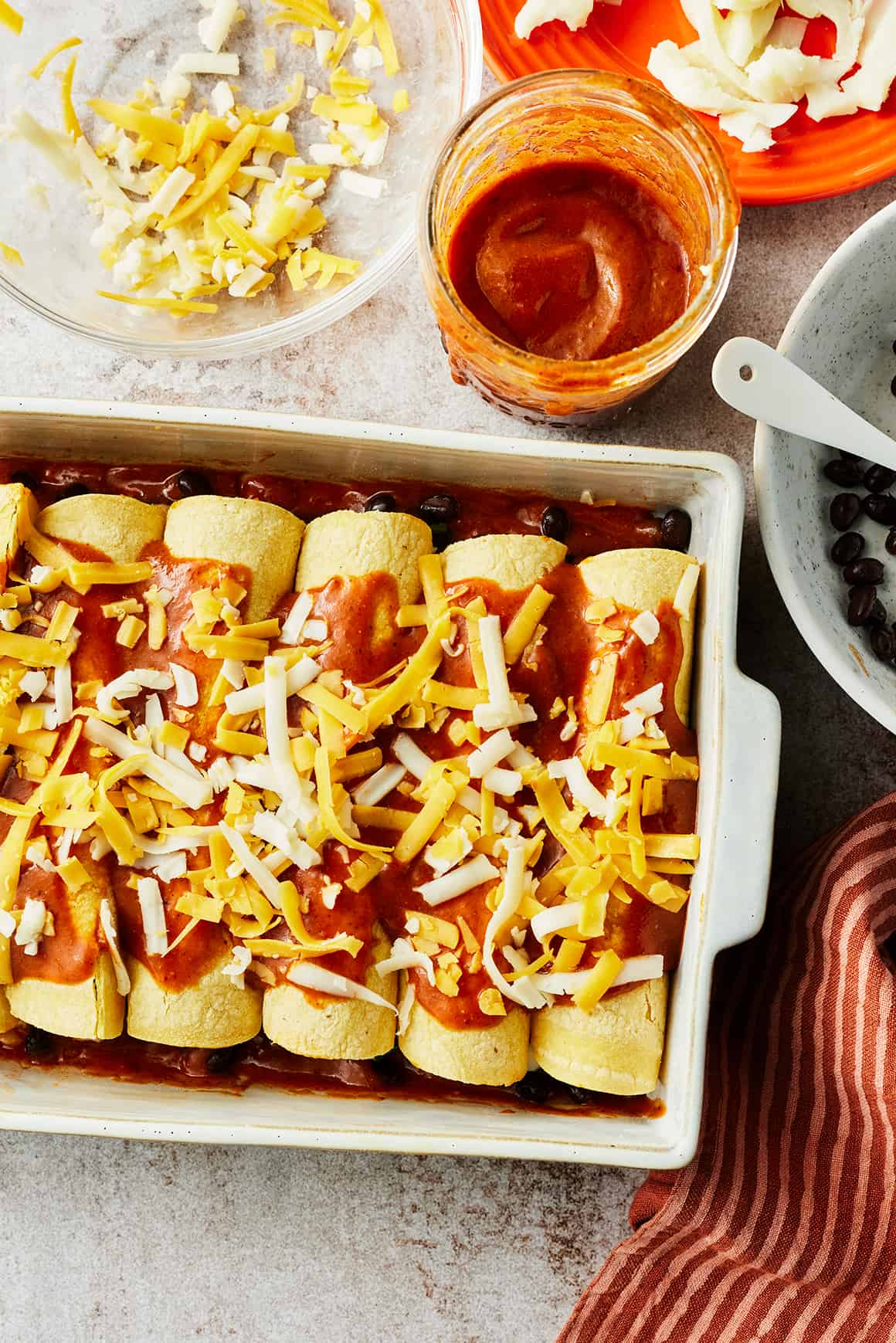 Enchiladas in a baking dish topped with red enchilada sauce and shredded cheese