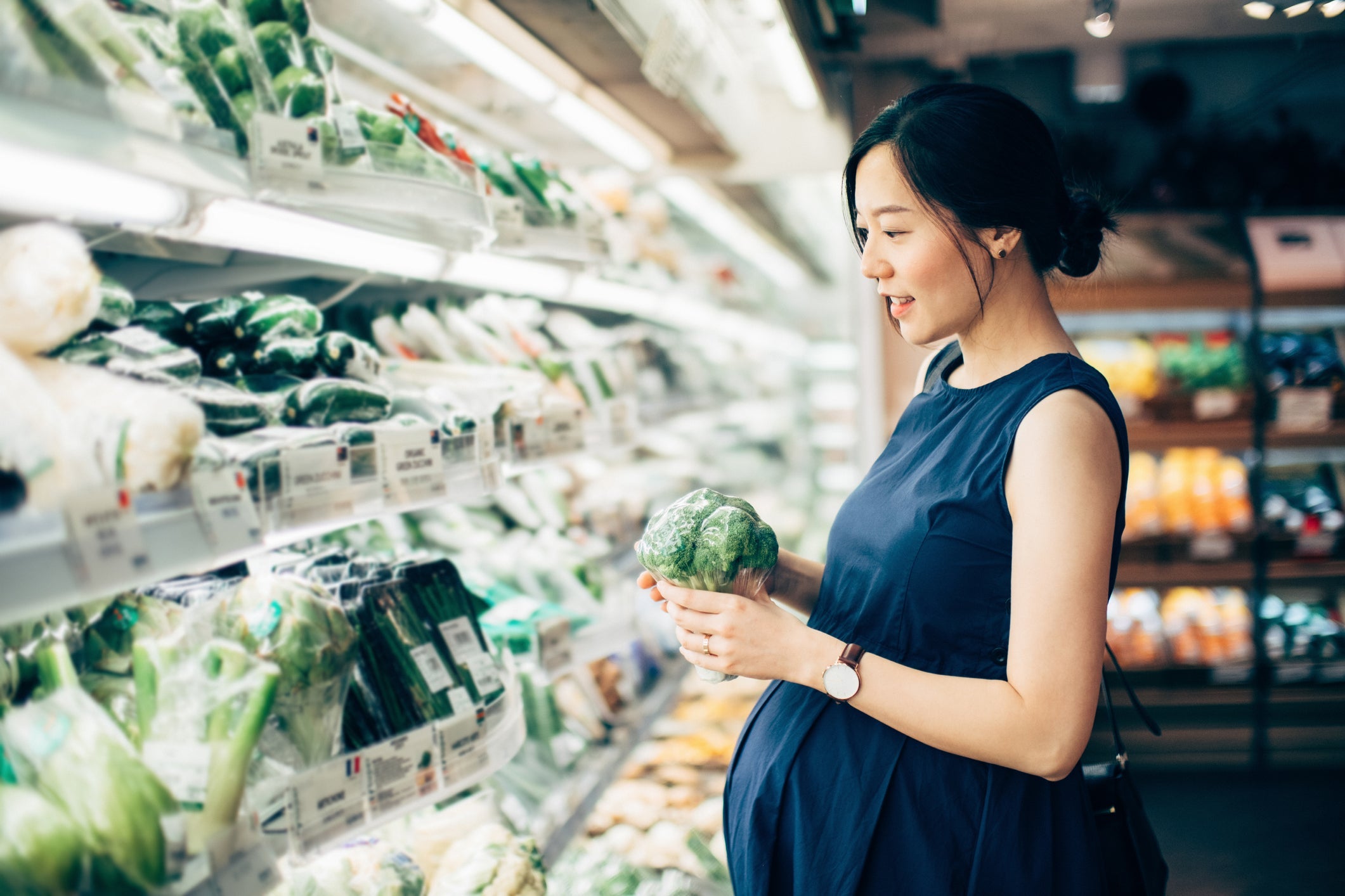Pregnant woman shopping for grocery in the fresh food aisle.