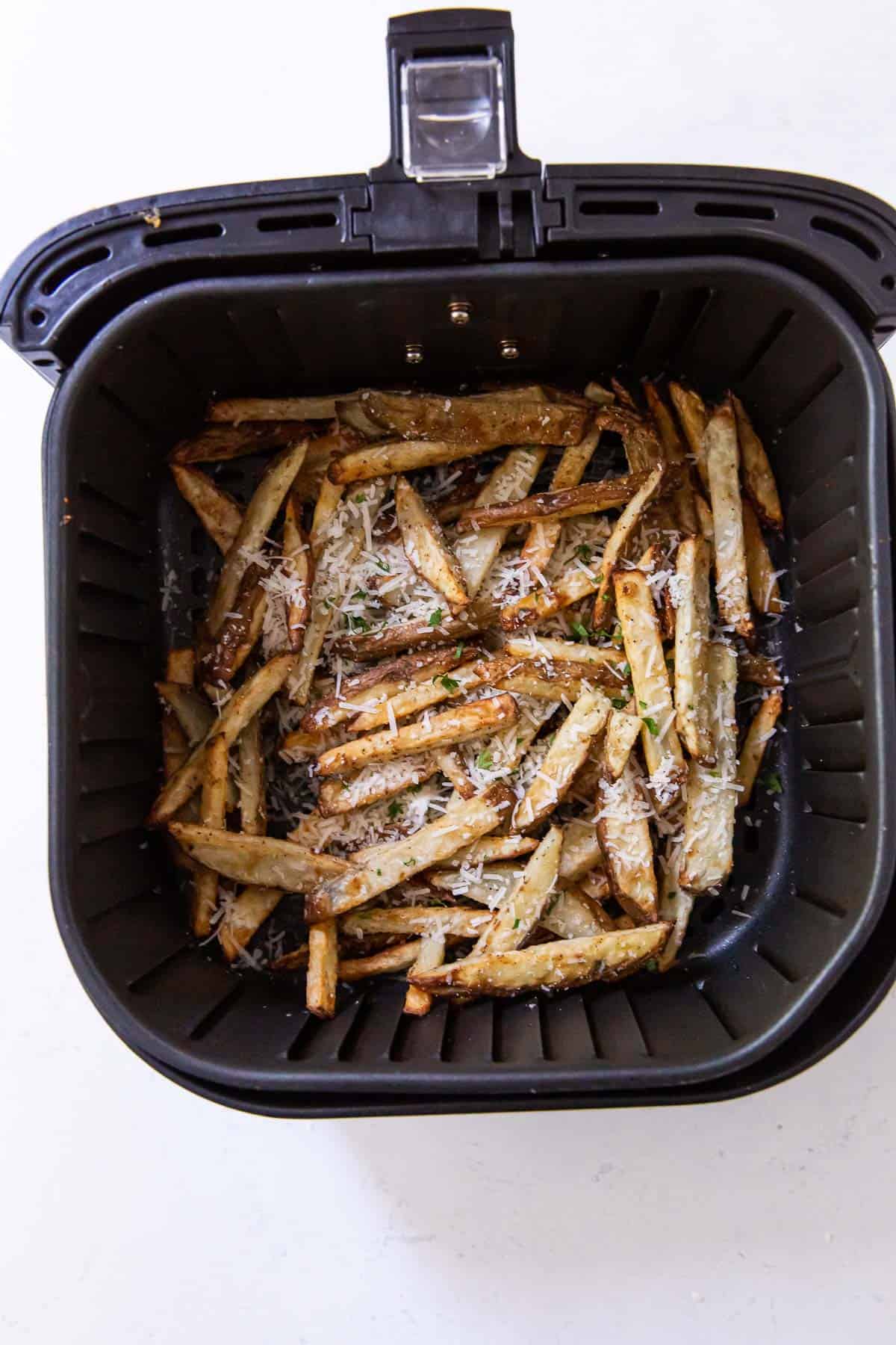 Potatoes in the air fryer layered with parmesan cheese.