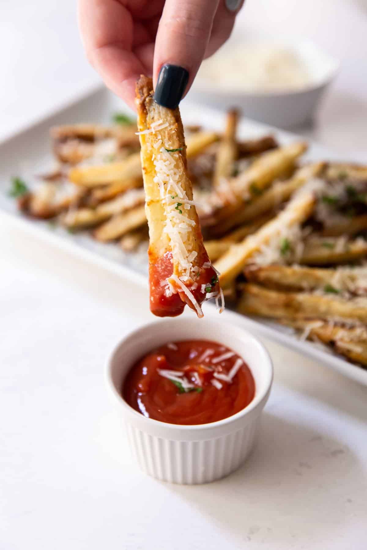 Fingers dipping french fries into ketchup.