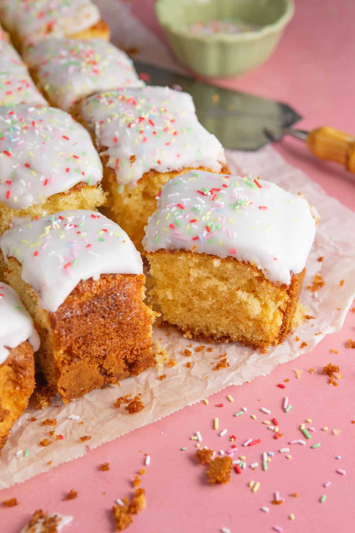 Squares of gluten free school dinner cake with thick white icing and rainbow sprinkles.