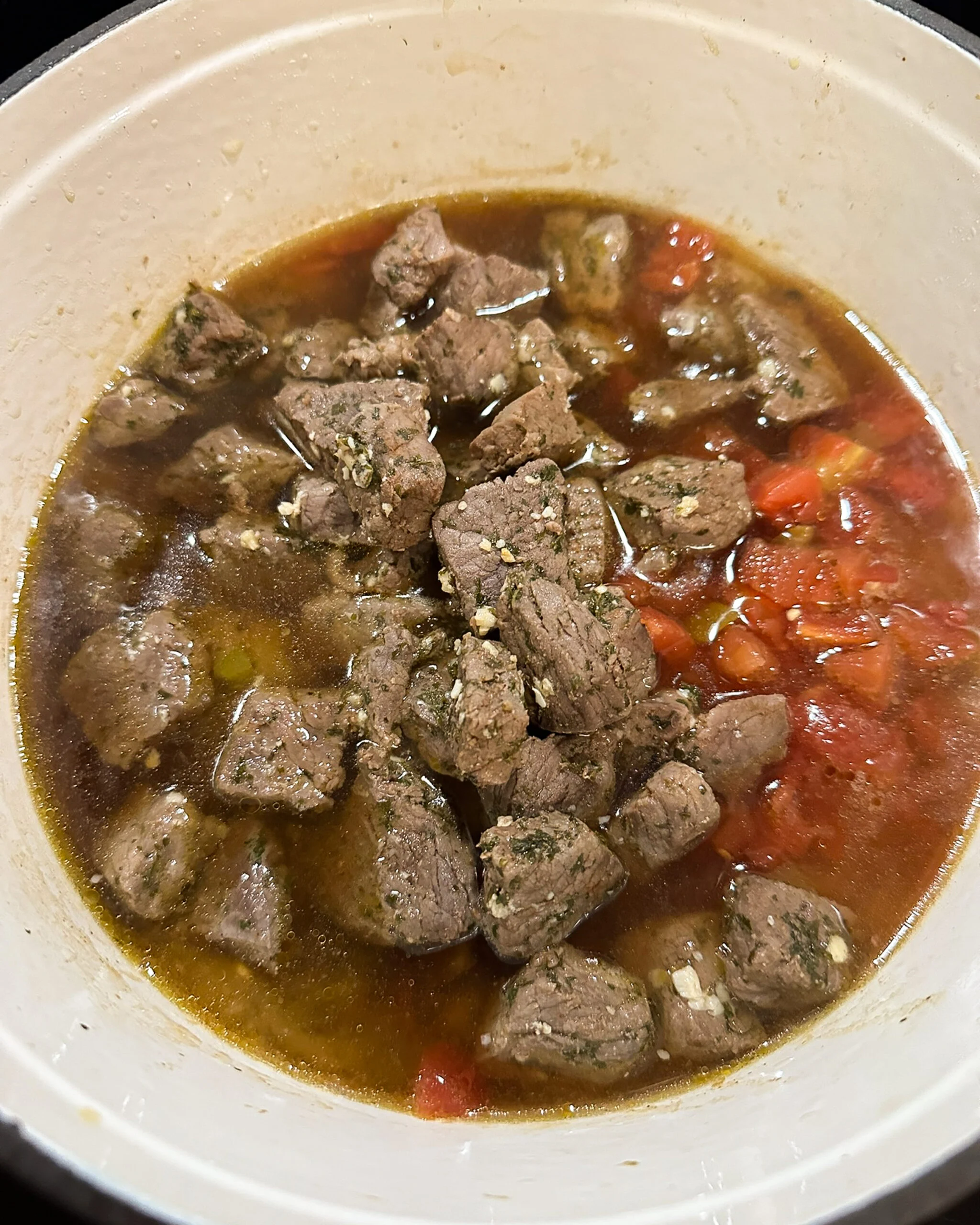 Browned meat, diced tomatoes with green chilies, beef broth, roux, and vegies in a pot during the last step of making grillades and grits.
