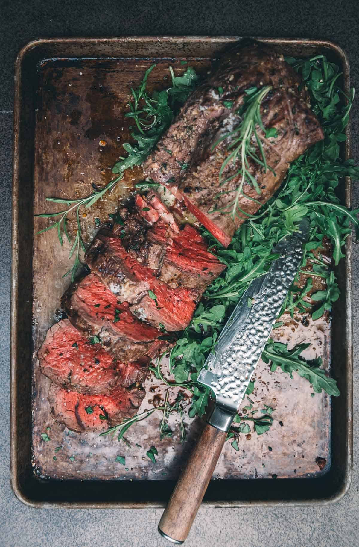 Beef tenderloin on serving platter with arugula.