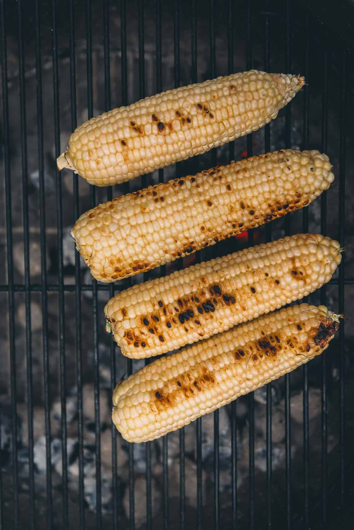 Corn with charred kernels on the grill grates over charcoal.