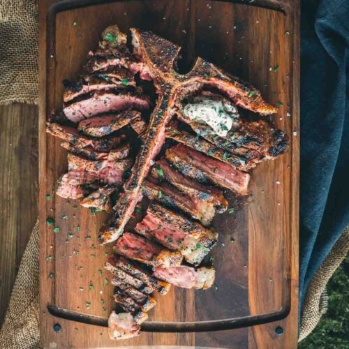A grilled t-bone steak on a wooden cutting board.