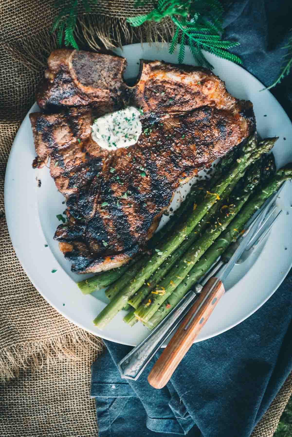Dinner plate with a large t-bone resting with compound butter and veggies. 