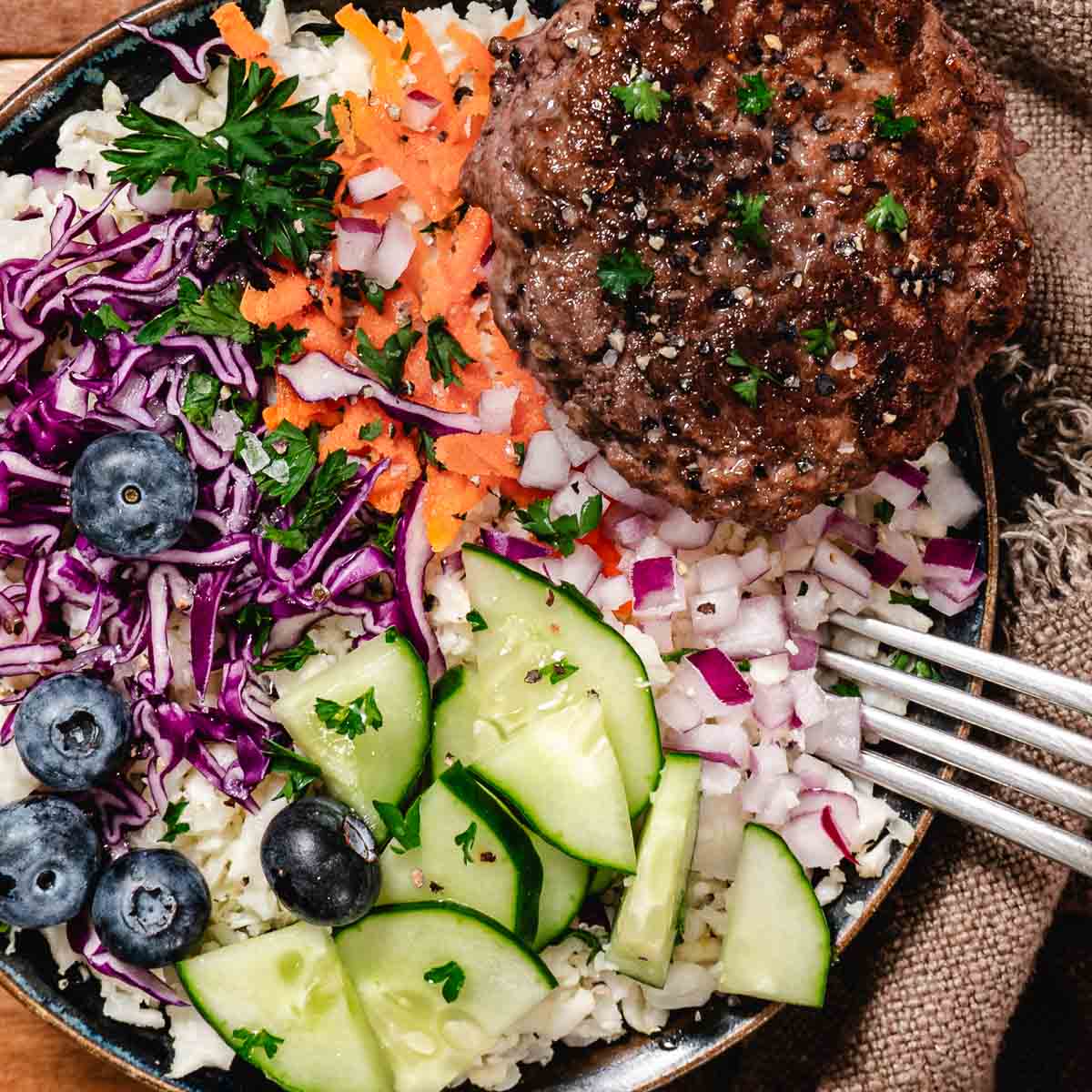 Veggie burger bowl with cauliflower rice, carrots, cabbage, cucumbers, red onions, parsley, and fresh blueberries.