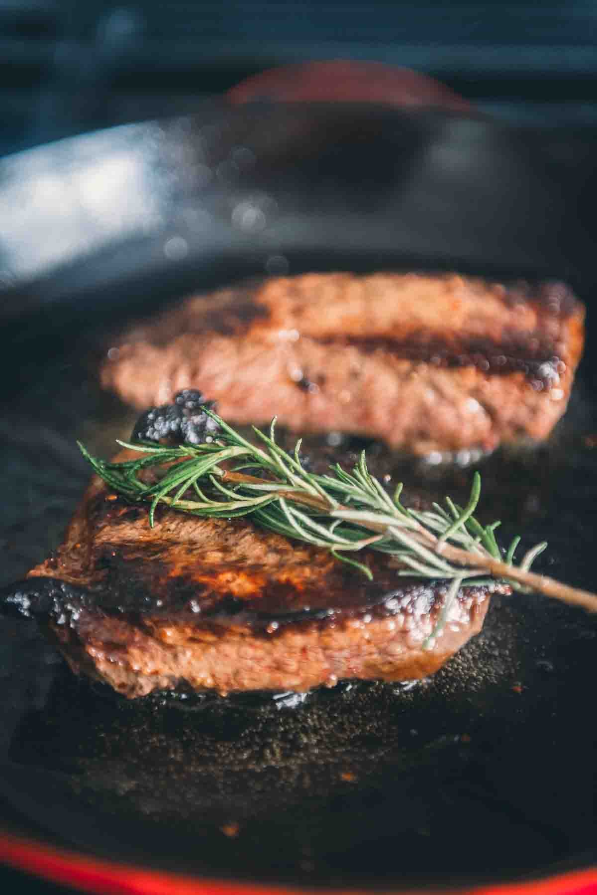 Flipped merlot steaks with rosemary on top in skillet. 
