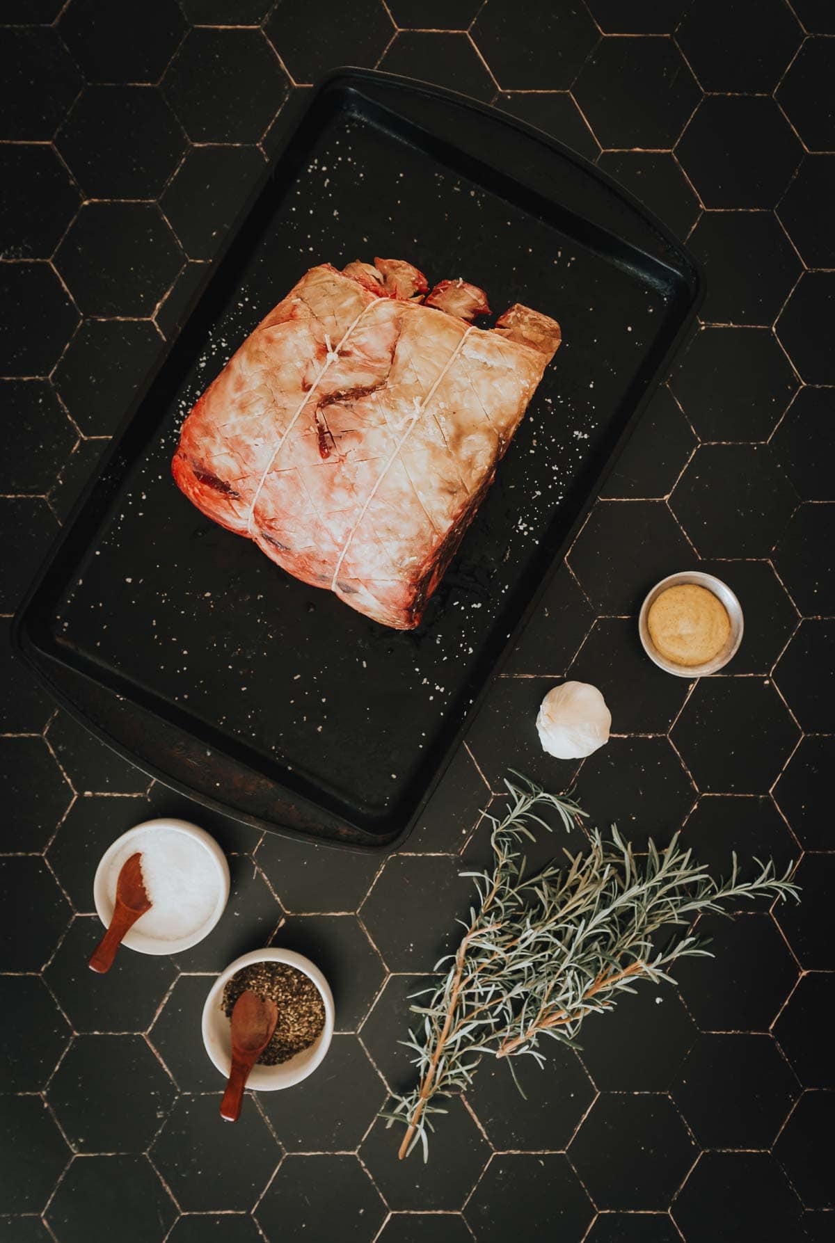 A standing rib roast on a baking tray with herbs and spices.