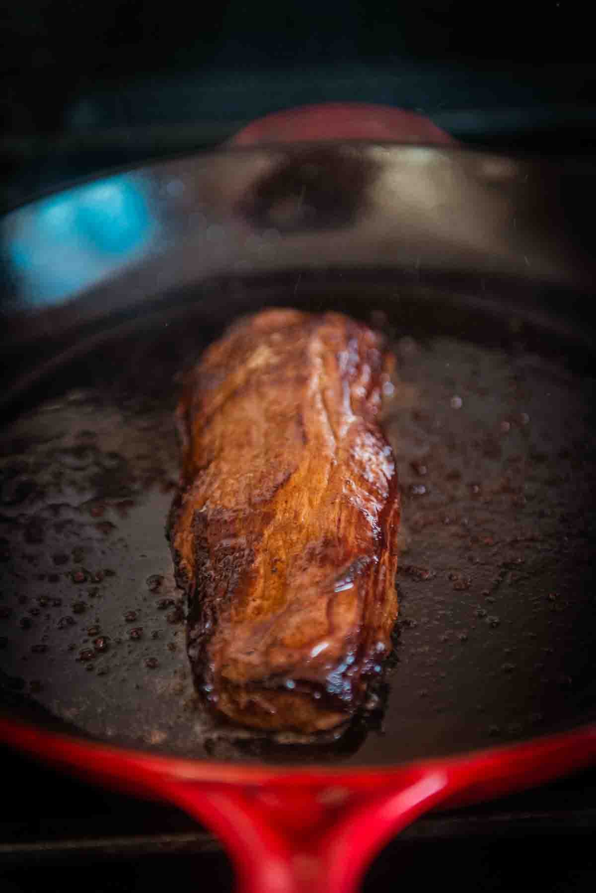 Steak seared and flipped to show the brown crust on top in the pan. 