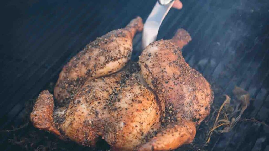 spatchcock chicken being removed from the grill.