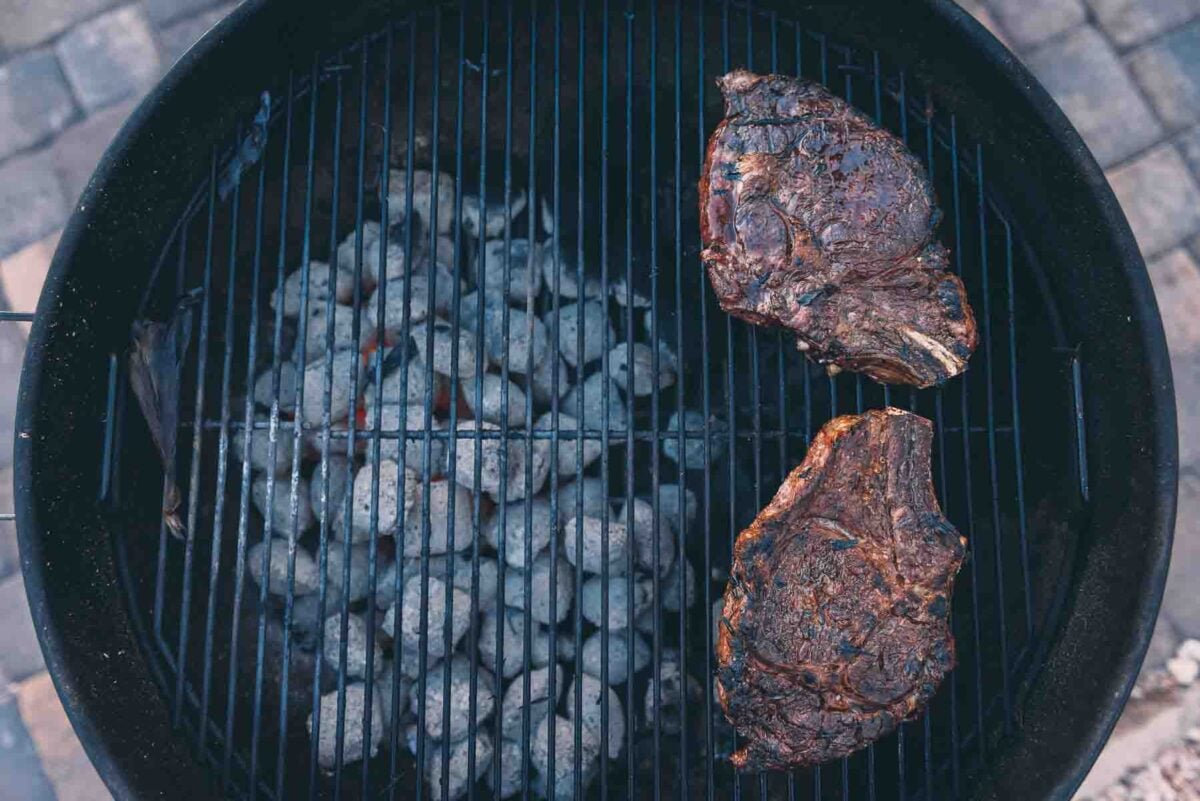 Showing bone in rib eye steaks over indirect heat on a charcoal grill, the cool side of the grill. 