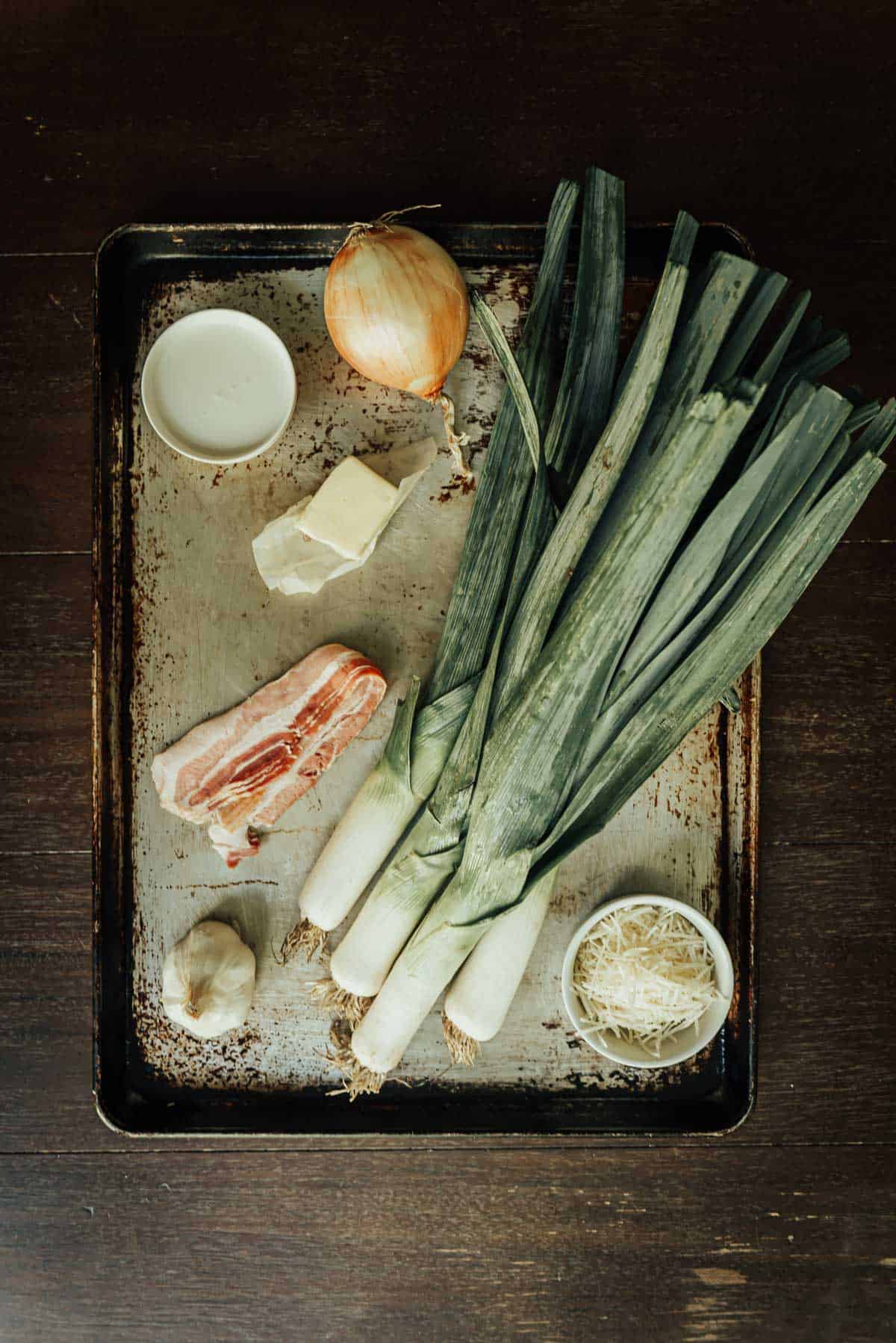 Leek, bacon, onion and garlic on a tray.
