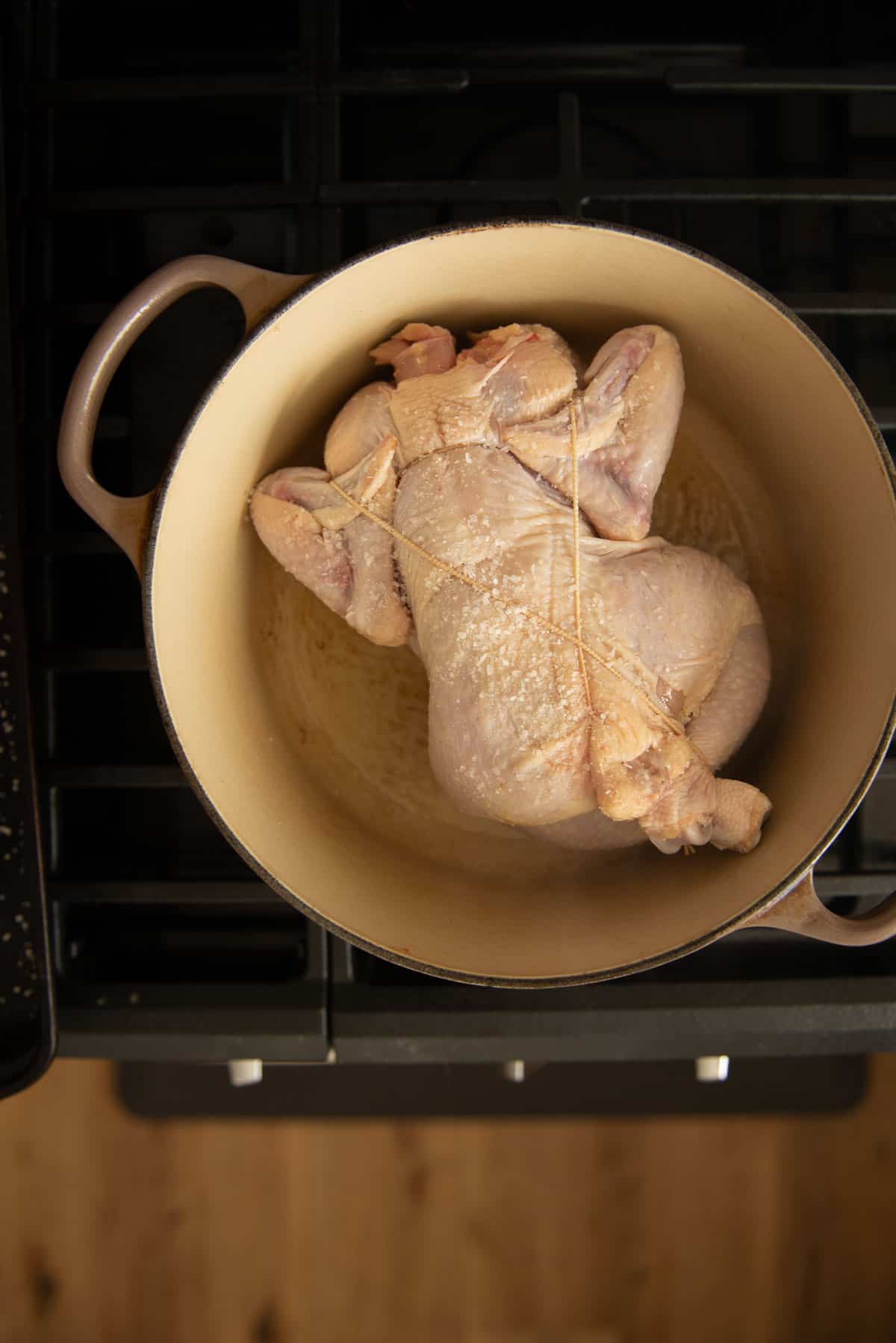 A chicken is searing, breast side down, in a Dutch oven on top of a stove.