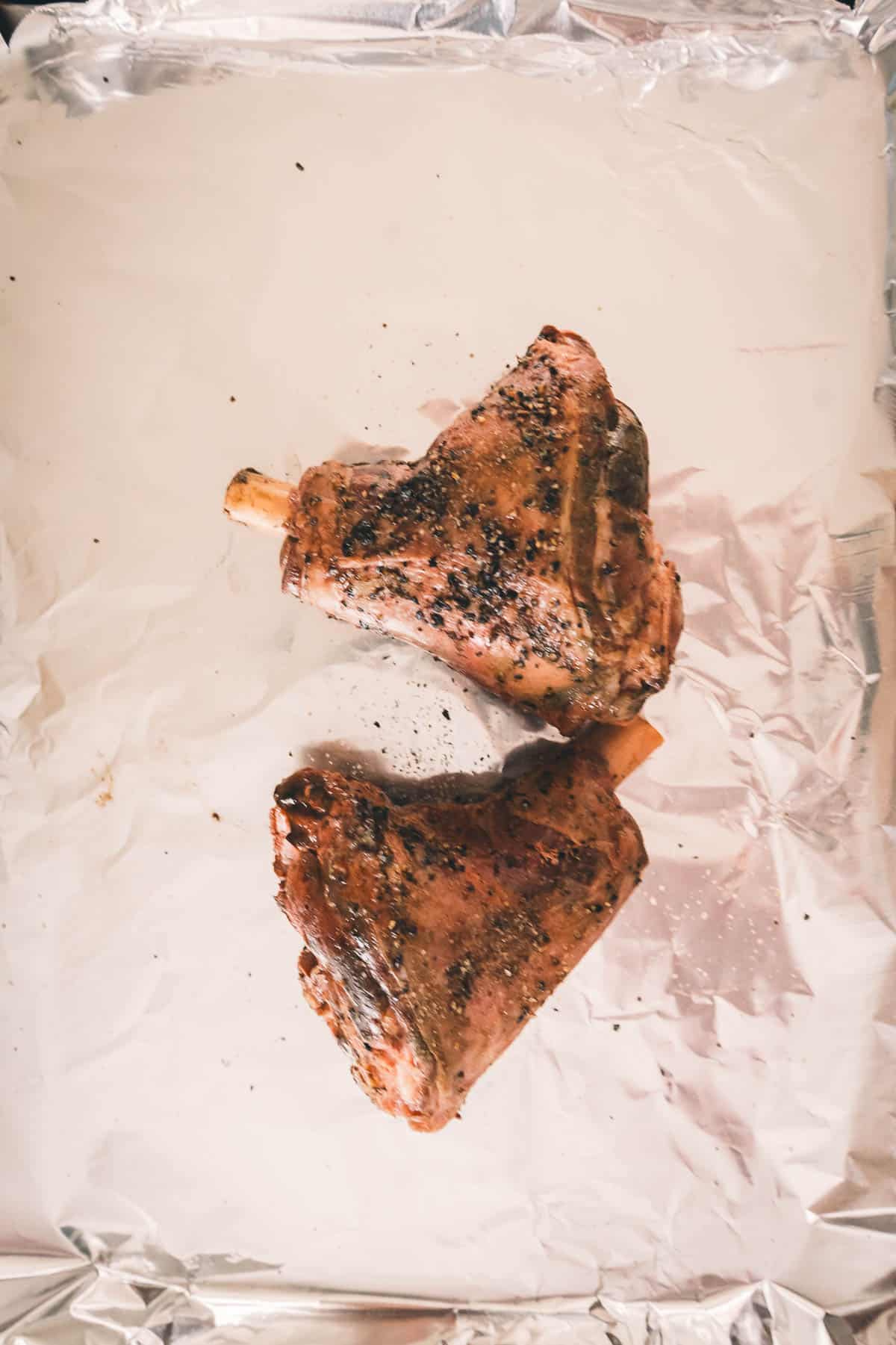 Two lamb shanks on a piece of foil ready to go into the oven.