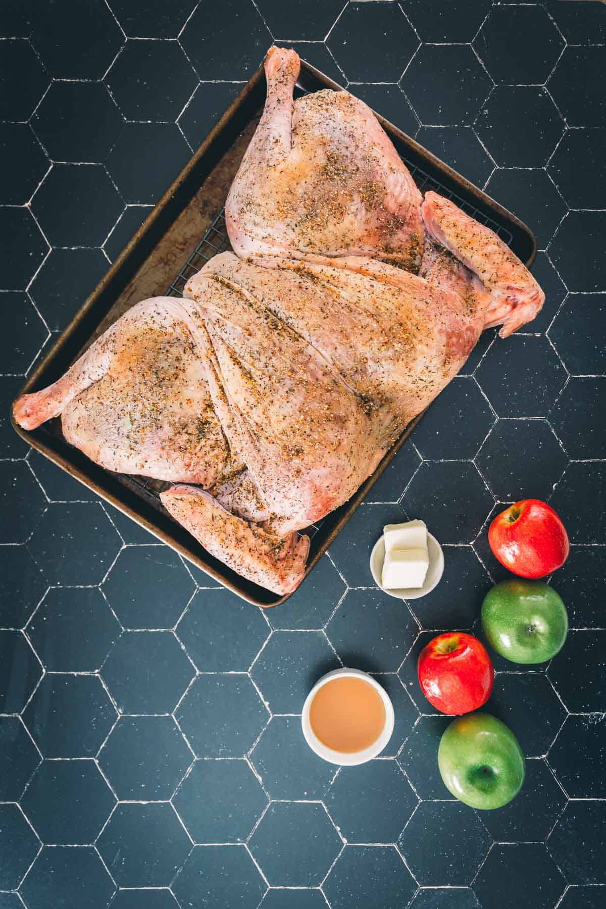 Turkey spatchcocked on a baking sheet with apples near by. 