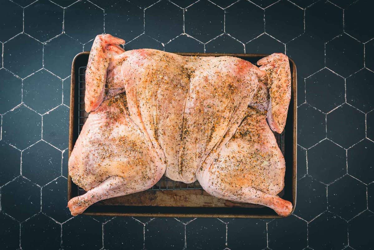 Raw spatchcocked turkey seasoned with salt and herbs on a roasting pan. 