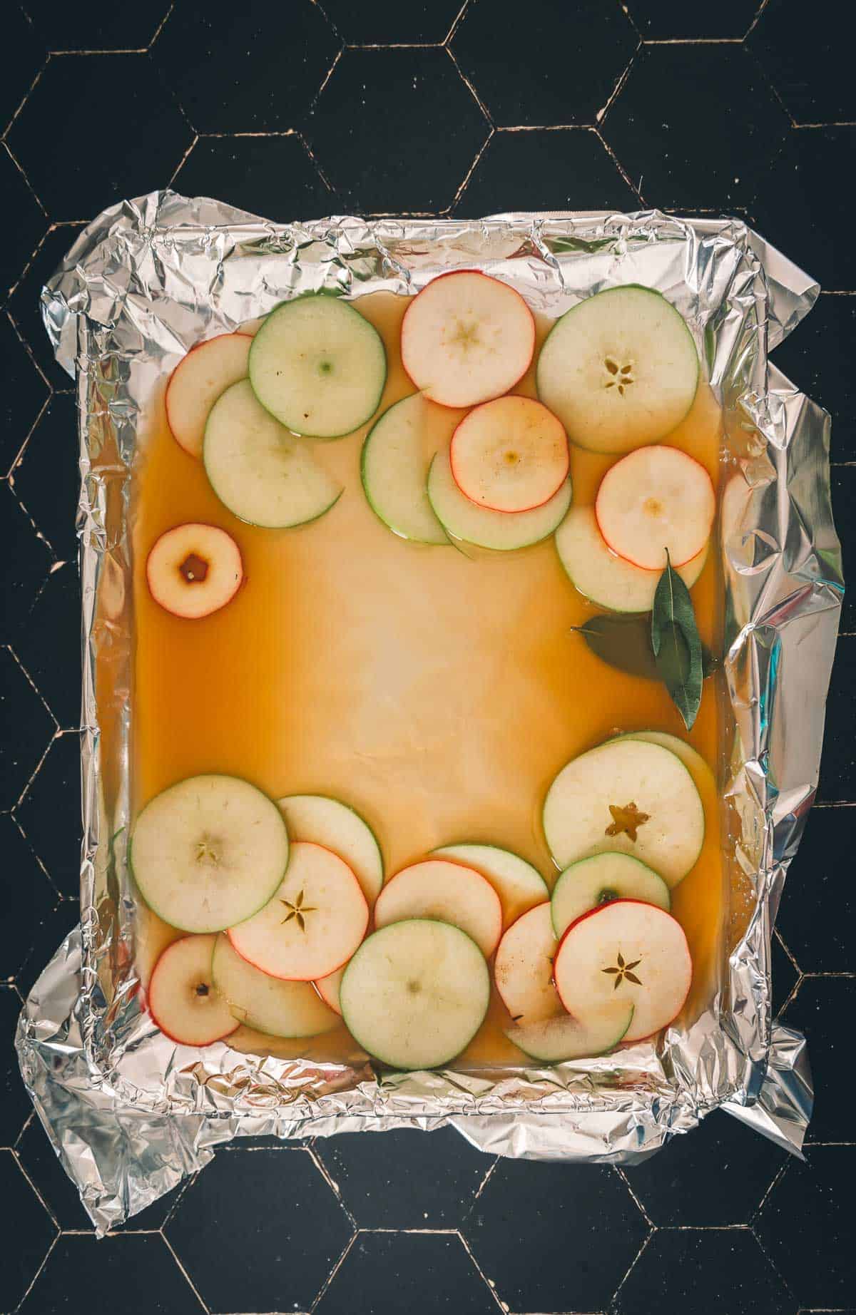 Apples sage and broth over foil on a baking sheet. 