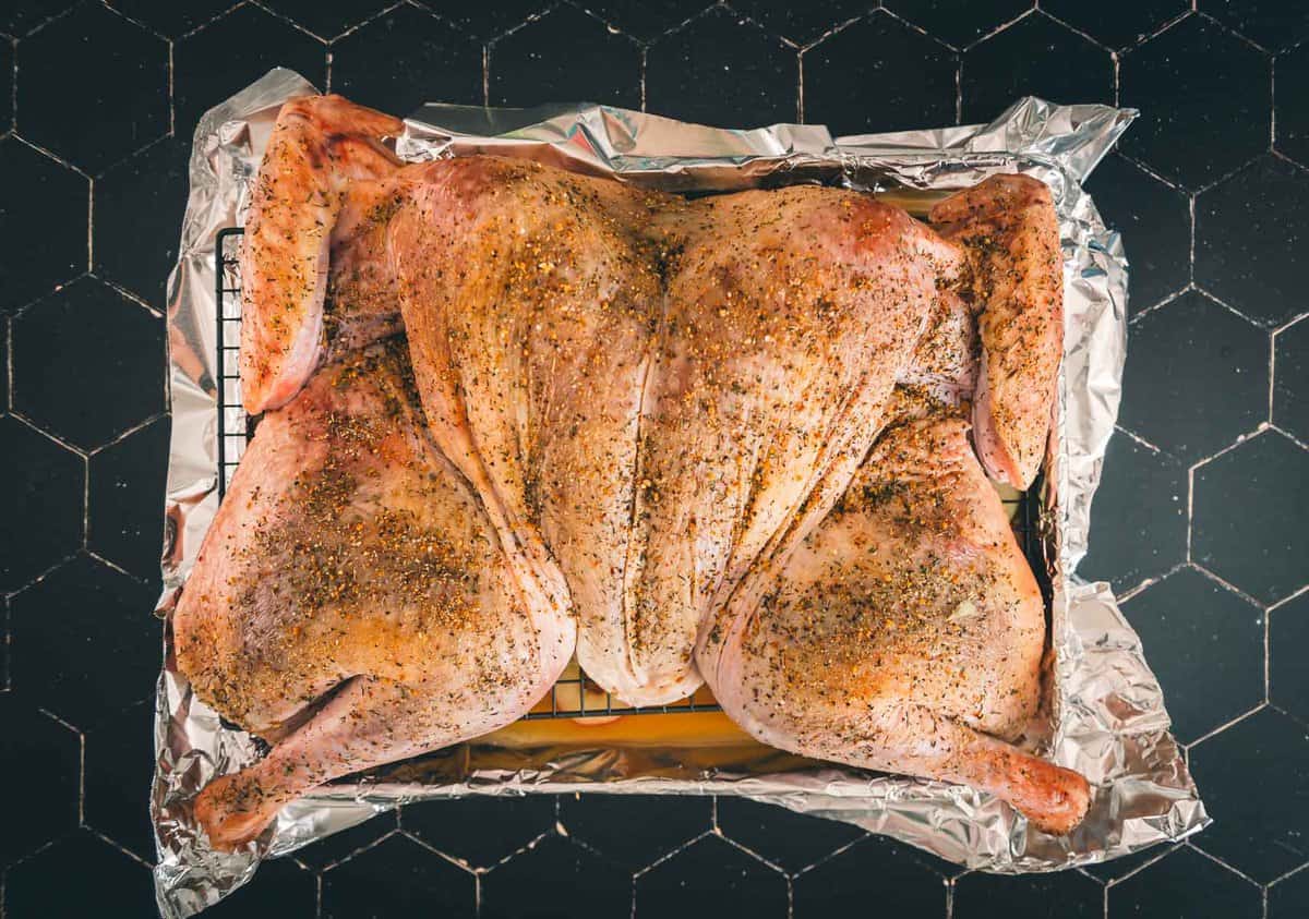 Seasoned spatchcocked turkey laid flat and ready to go in the oven.