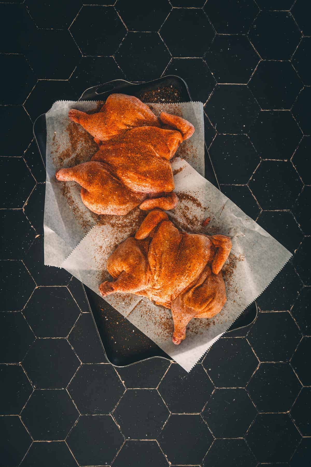 Seasoned game hens on a baking sheet.
