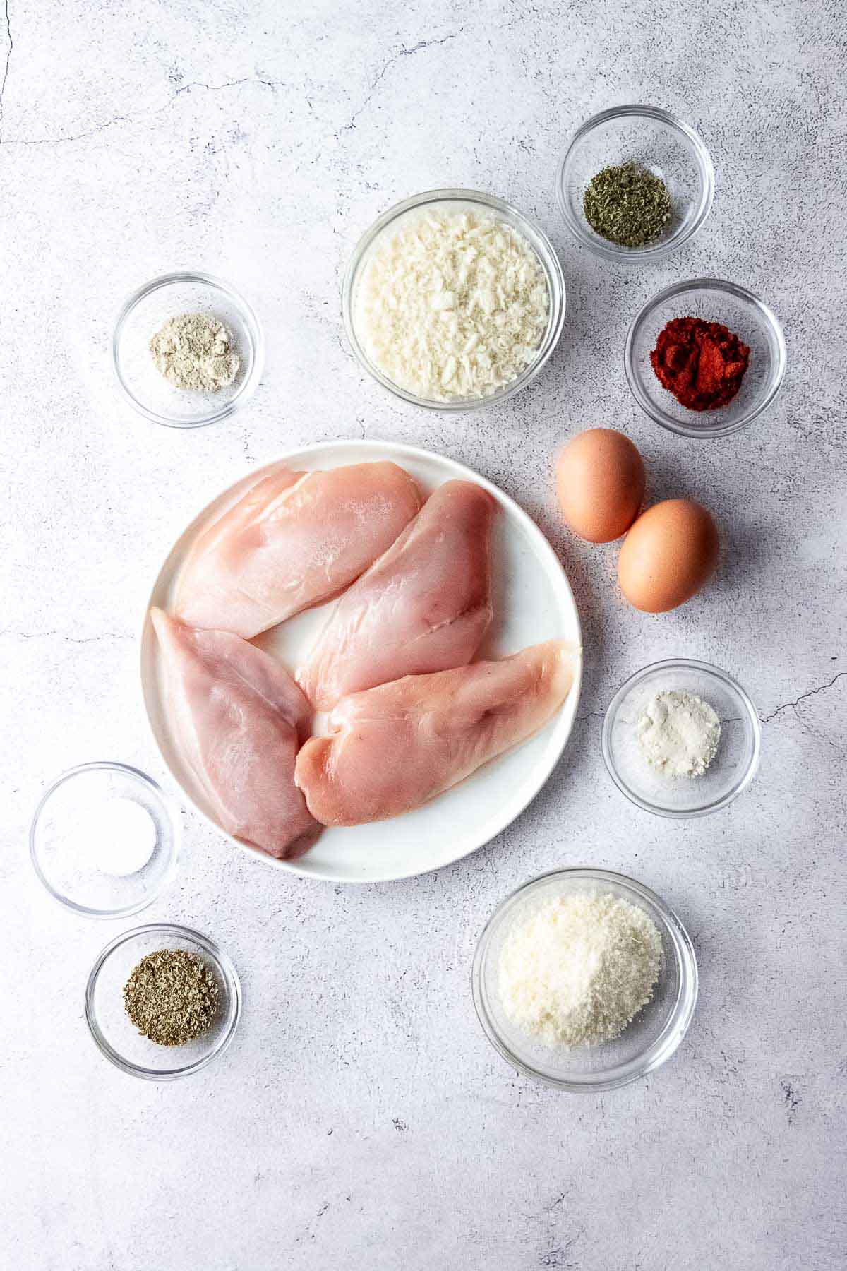 Panko crusted chicken breast ingredients on a white plate.