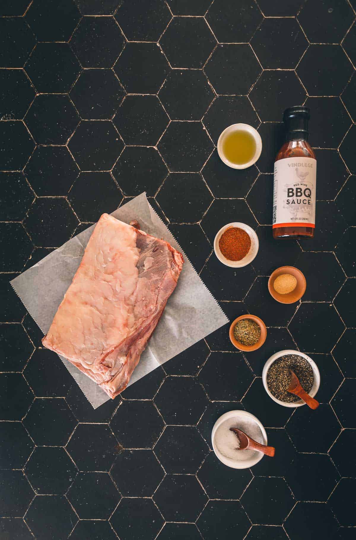 A rack of lamb ribs, spices, and seasonings on a black table.