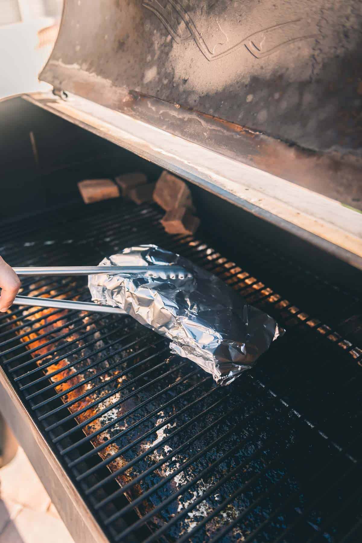 A person holding a wrapped ribs returning them to a bbq grill.
