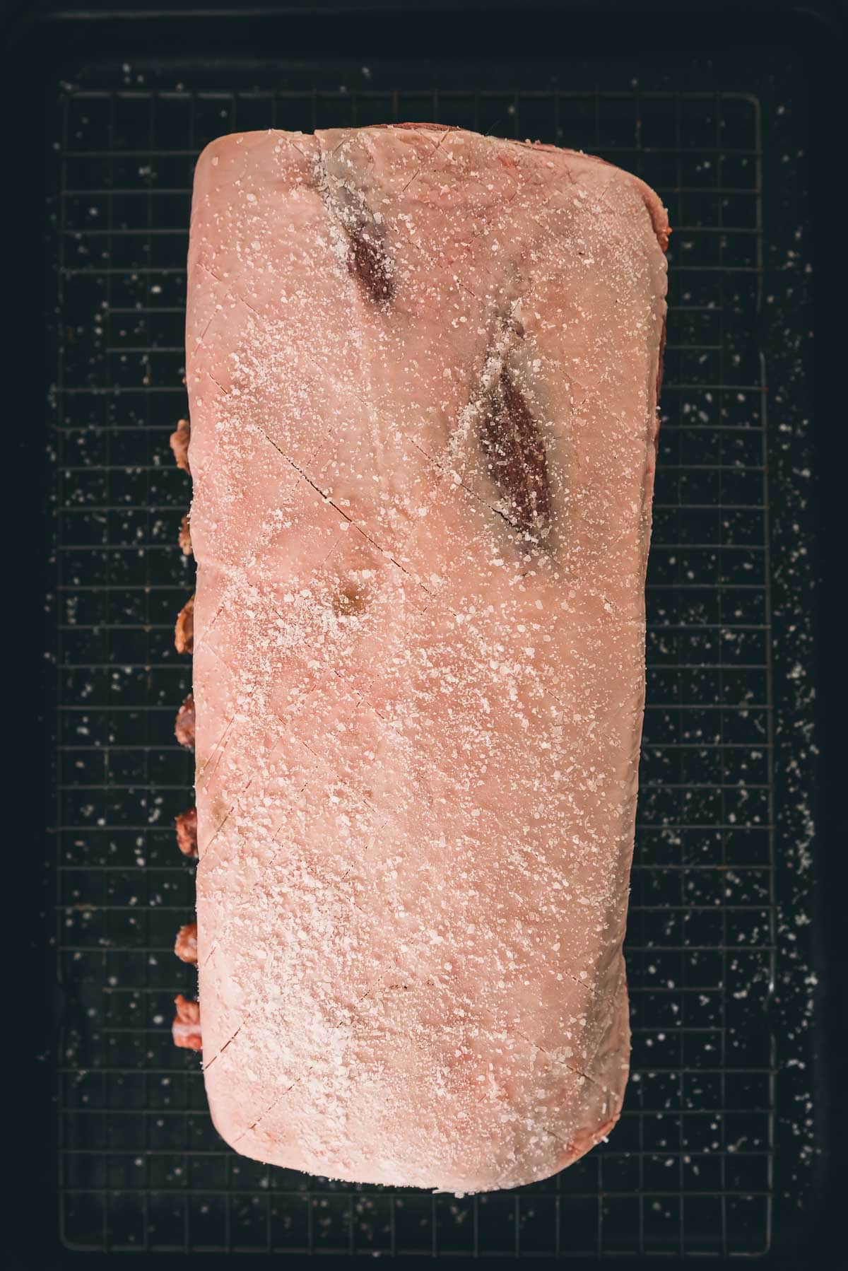 Showing the scored and salted fat cap on a rack of pork.