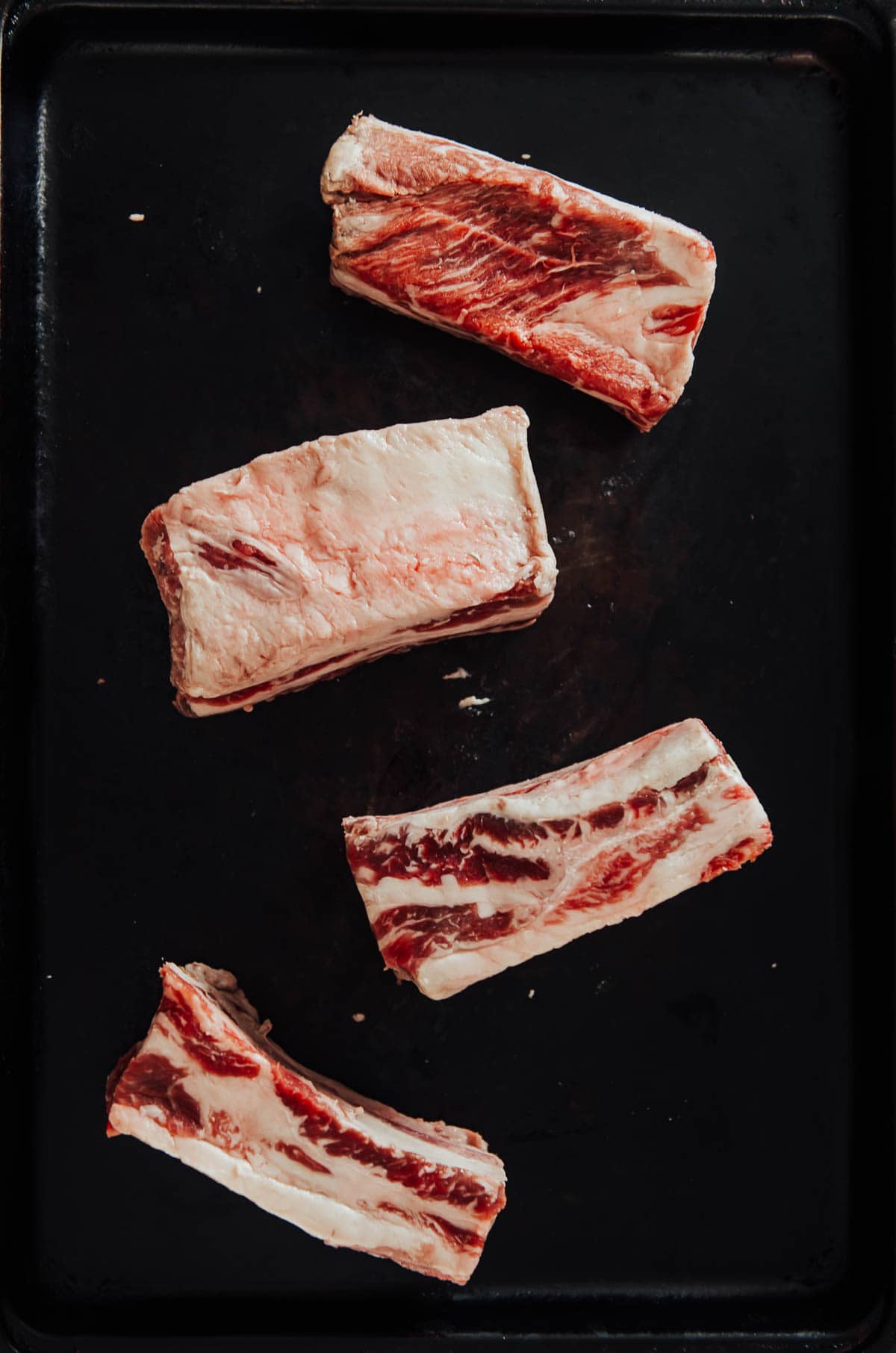 Four bone-in short ribs on a baking sheet.