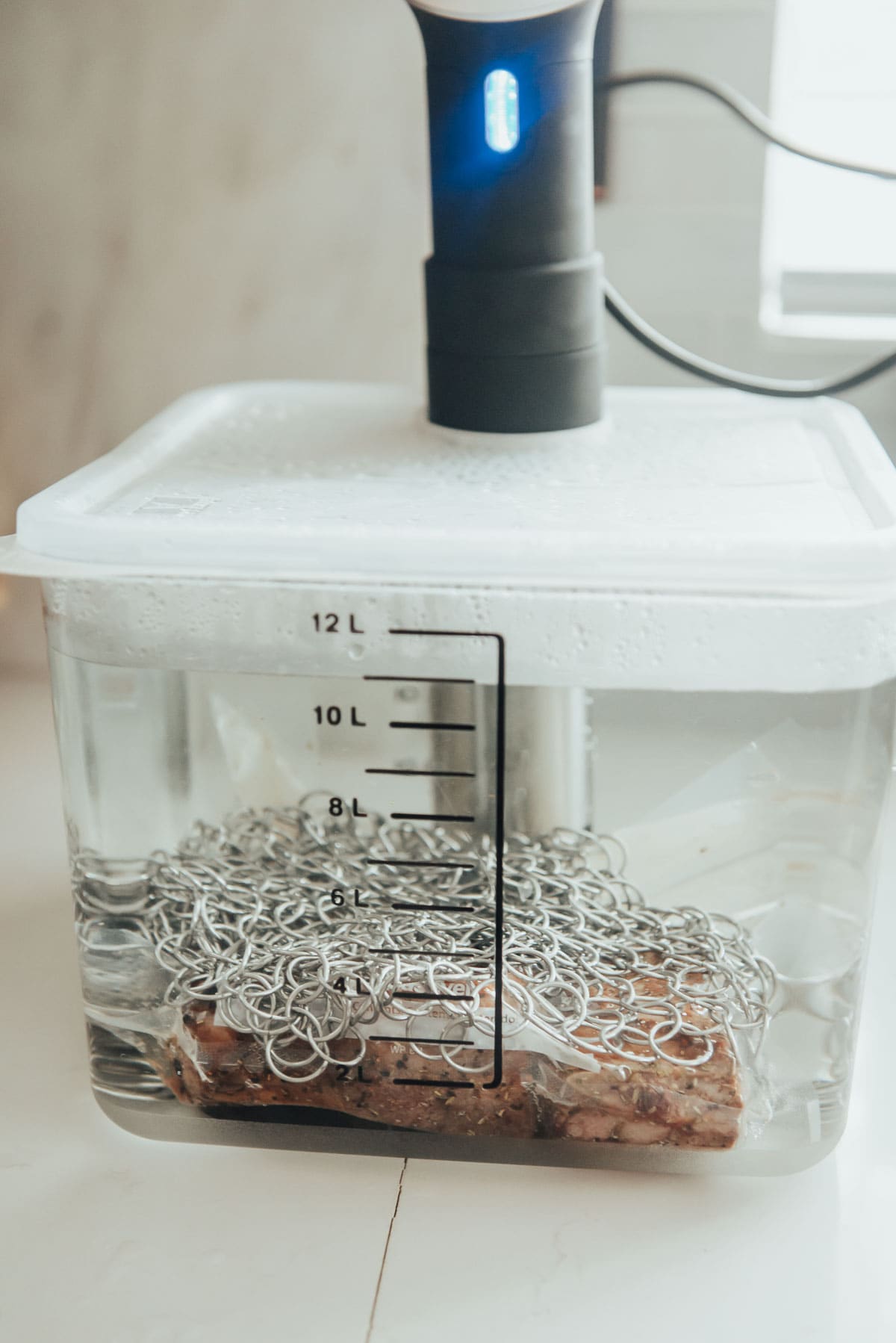 A container of water bath and beef ribs submerged.