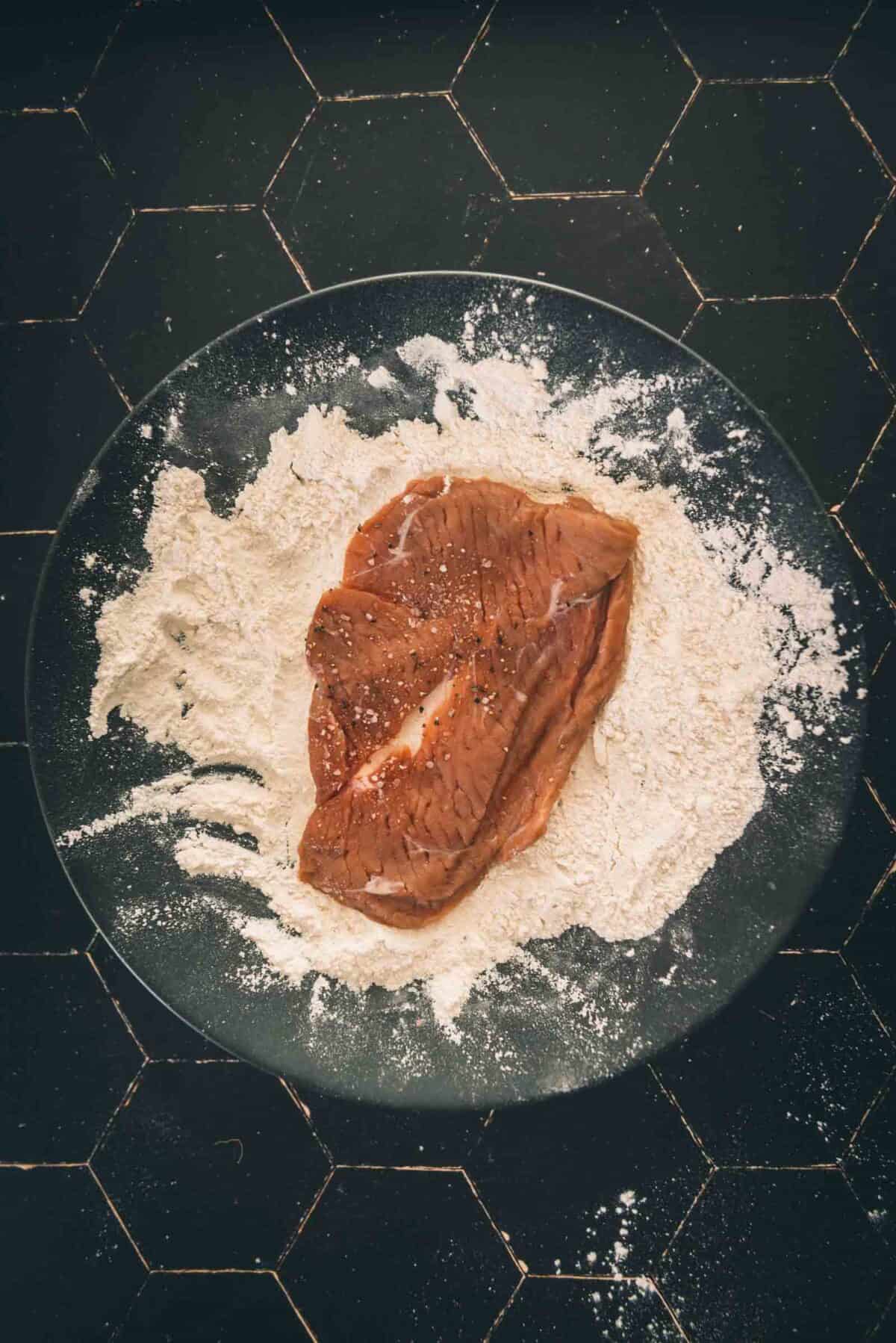 A piece of veal on a plate with flour on it.